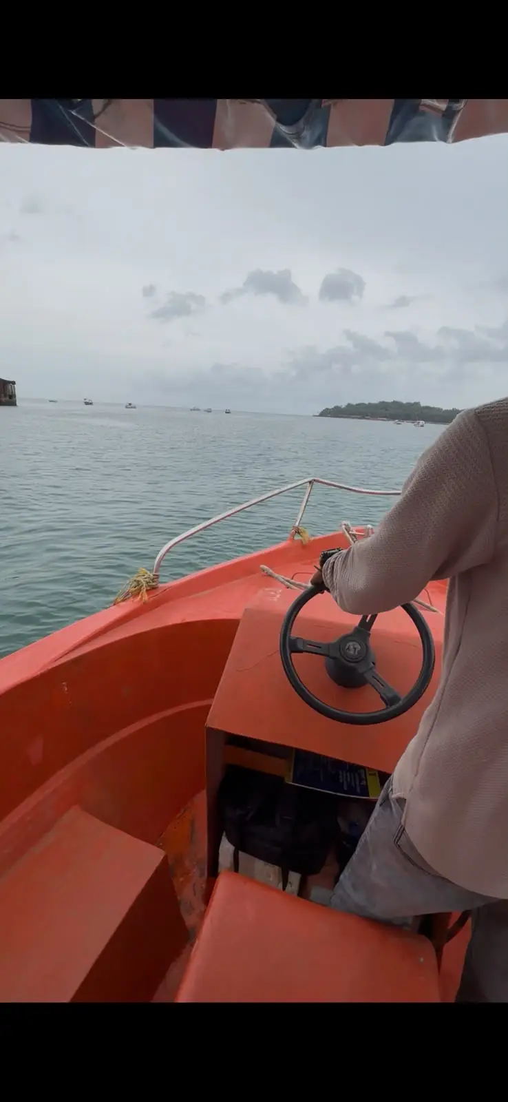 View from a small orange boat crossing the bay toward the seaweed farm, with the shoreline in the distance.