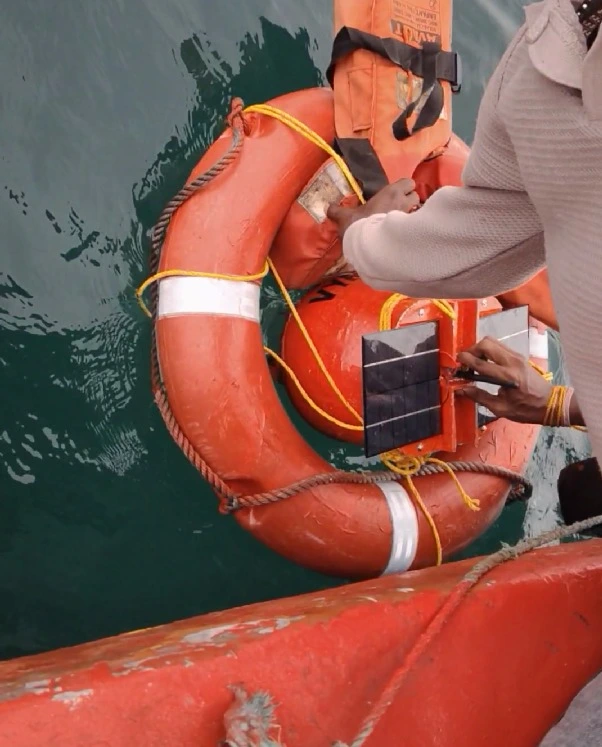 Close view of the buoy's solar panel and orange float being handled at the water's surface.